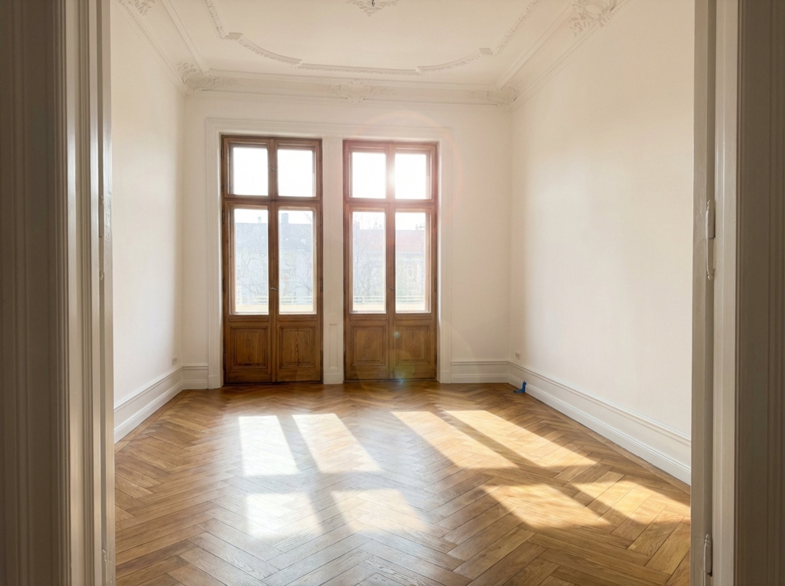 Leerer, geräumter Altbau-Raum mit Parkett und großen Fenstern